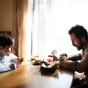 A man sitting at the kitchen table with his son after being unemployed for many months.