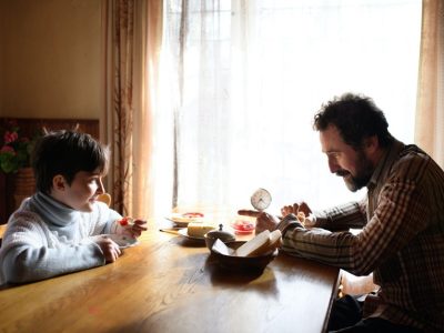 A man sitting at the kitchen table with his son after being unemployed for many months.