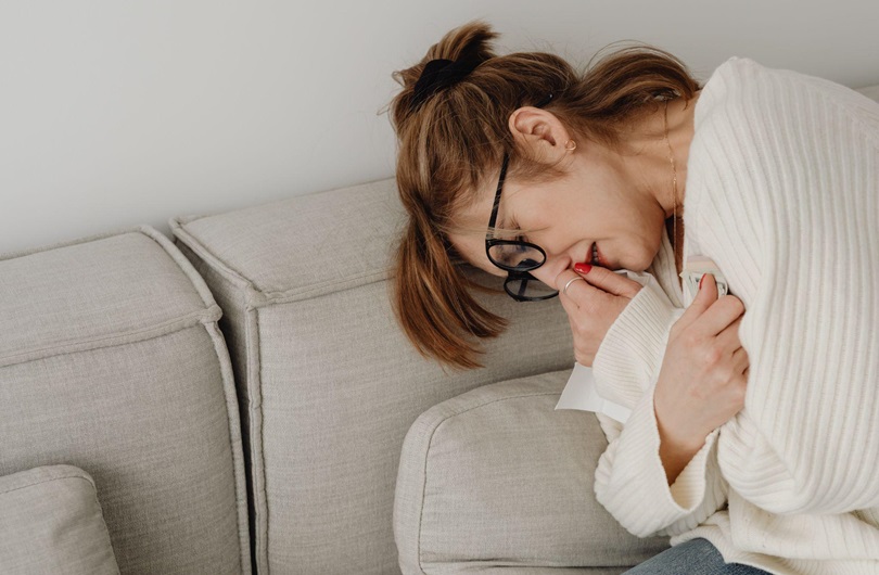 An overwhelmed woman crying on the couch because of crippling unemployment.